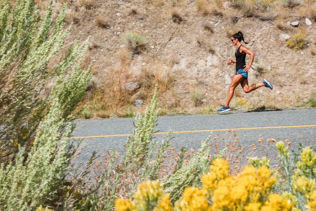 Runner jogs along the roadside near wildflowers and tall grasses.