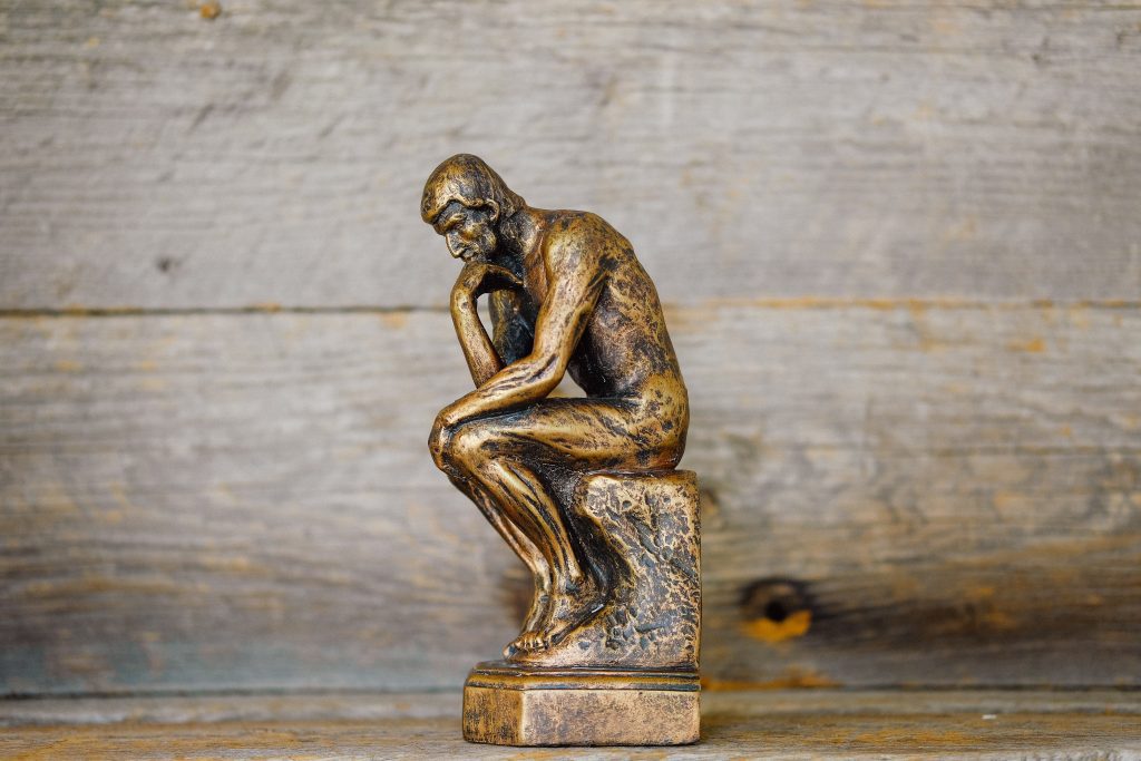 Rodin pewter statue of the thinker sitting on a wood desk with wooden paneling in the background contemplating modern day work life.