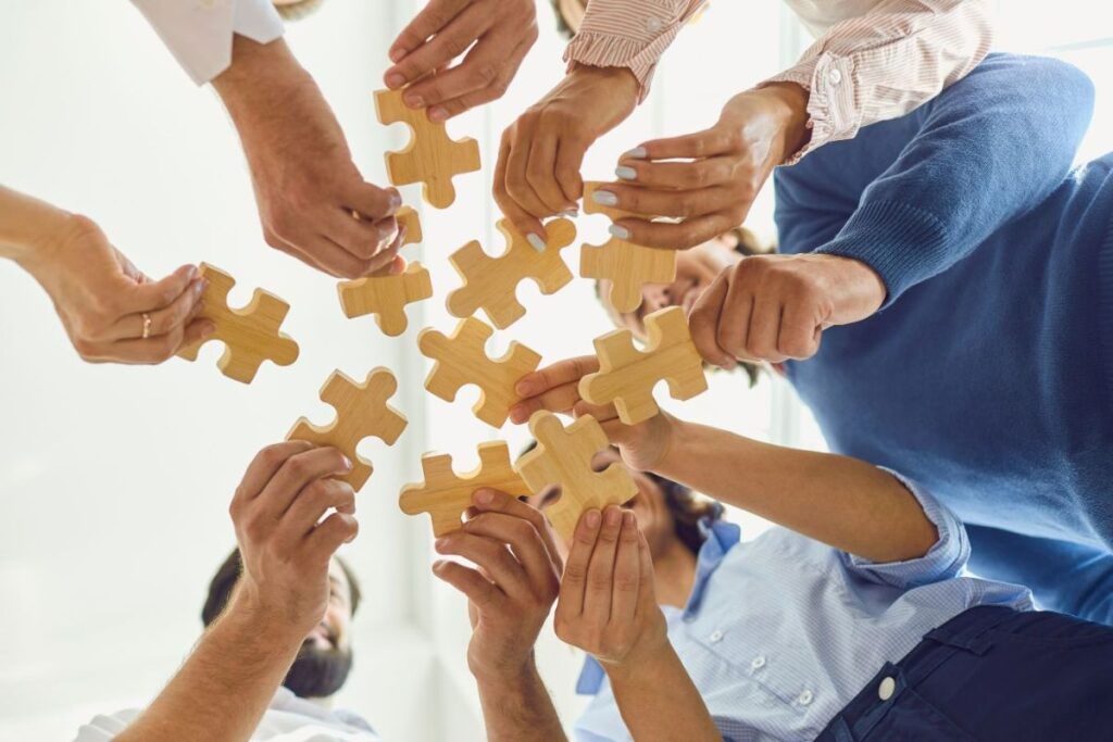 employees working together to fit wooden puzzle pieces together as a symbol of working together to solve problems and be a positive part of a team. 