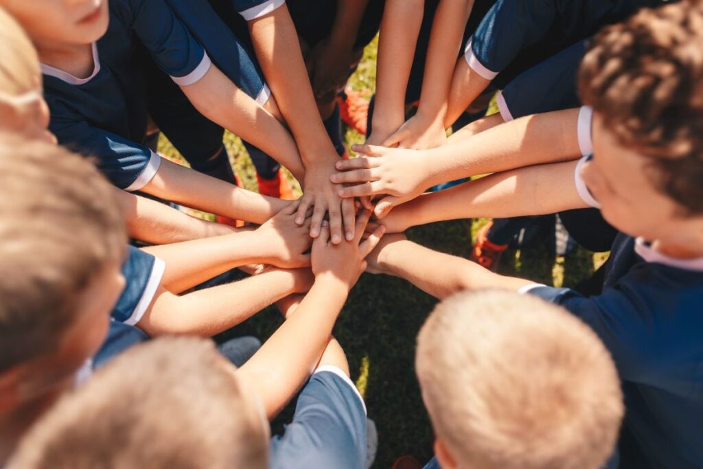 Youth arms and hands of a kids sports team stacking hands in the center of a team circle or huddle to represent teamwork and working together to build a stronger and more effective team.