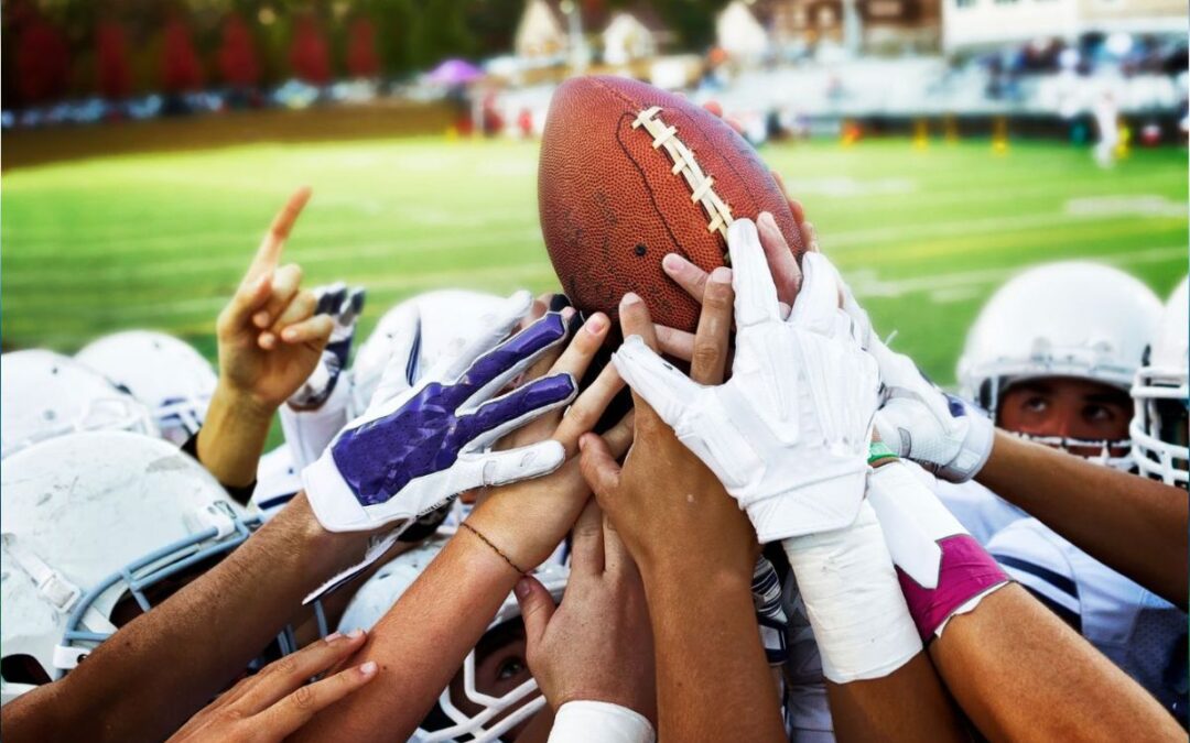 A team of hands reaching toward a football as a symbol of teamwork and learning how to build better teams