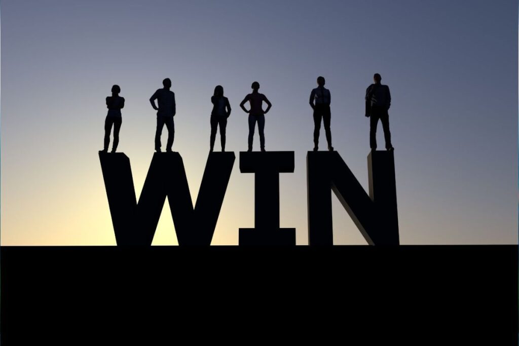 silhouette of a group of team members standing on top of oversized letters that spell out WIN indicated the desirable outcome when employees work together as a team.